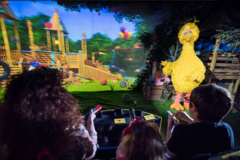 guests riding by a screen with a playground and a big yellow bird on Sesame Street: Street Mission dark ride - PortAventura World, Salou, Spain