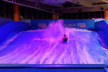 person surfing on illuminated water wave in vibrant hue of magenta on the FlowRider Surf Machine, Splash Lagoon Indoor Water Park, Erie, Pennsylvania, USA