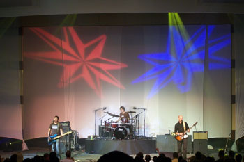 yellow beams of light above stage with red and blue eight pointed star gobos side by side on wall behind Tree63 bandmembers playing on stage - Apopka, Florida USA