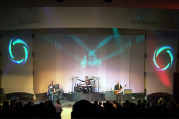 red wash on side of stage with aqua blue round gobos on each side of stage and beams of aqua blue on wall behind Tree63 bandmembers playing on stage - Apopka, Florida USA