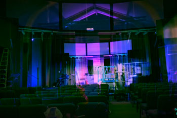 view of stage with instruments illuminated with vibrant colors of magenta and blue from Techni-Lux UltraLux 7 LED - 6in1 RGBWAUV fixtures and installation equipment in front of stage inside City View Church stage - Renton, WA, USAA