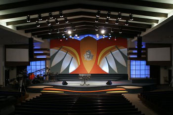 video monitors screens on far side walls, center stage styalized dove in painted hue of orange, red, yellow, black and white translucent panels with dimmed blue LED behind it , International Tabernacle, West Palm Beach, FL, USA