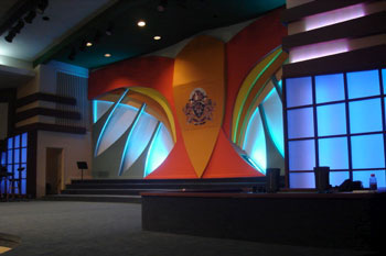 angle view of stage styalized dove in painted hue of orange, red, yellow, black and white with 		aqua blue LED wash in the feathers translucent panels with vibrant blue purple LED wash LED 		behind it , International Tabernacle, West Palm Beach, FL, USA