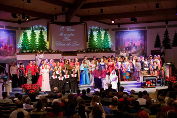 scene with white snowflake gobo patterns in front of  christmas trees with white lights on angels on back row and choir in front with woman dressed as mary holding baby jesus in Journey to the Manger Musical - South Orlando Baptist Church, Orlando, FL, USA