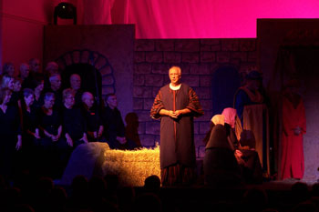 close up of actor withs spotlight on him on stage dressed as inkeeper with stage props of hay and                                 building set and SGM Palco red/pink LED wash on backdrop, Southpointe, Leesburg, FL, USA