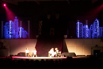 people sitting at tables with cityscape gobos behind on wall and red beams of LED light on stage of Your Final Destination - Victory Church, Lakeland, FL, USA