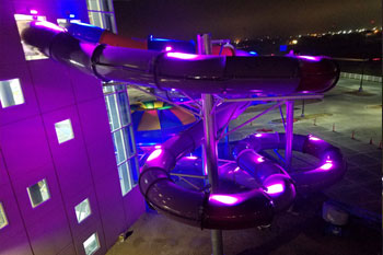 exterior section of water slide connected to interior of building and illuminated wtih vibrant purple led lights at Parrot Cove Indoor Water Park, Garden City, Kansas, USA