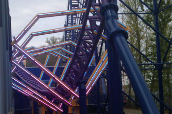 blue rollercoaster tracks going through yellow diamond shaped metal structures with mounted lit LED Pulsar Chromastrip fixtures with vibrant blue and red colors on the Bizarro Coaster Thrill Ride, Six Flags New England - Agawam, Massachusetts, USA