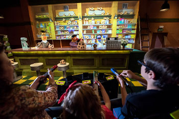 guests riding by a cafe shop with chocolate chip cookies on display and baked goods on shelves with characters behind the shop counter on Sesame Street: Street Mission dark ride - PortAventura World, Salou, Spain