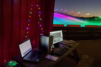 alpine village red wall with a strand of multicolored LED holiday lights in the shape of a triangle hanging on it and below a brown wooden picnic table with 2 laptop computers programming the lights and music for the LED light show on Snow Slopes at Snowcat Ridge Alpine Snow Park - Dade City, Florida, USA