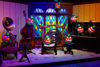 green humbugs playing instruments in music room illuminated stainglass window prop with hues of purple, yellow, green, blue interior scene of The Great Humbug Adventure Dark Ride - Santa's Village, Jefferson, New Hampshire, USA