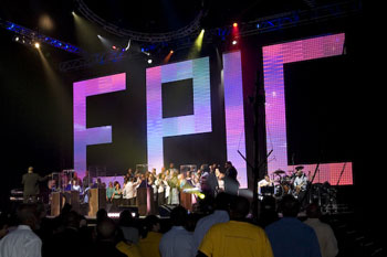 a crowd in front of the stage with musicians performing and behind them a huge backdrop of intensly bright and colorful LED lit individual letters that spell out the word EPIC at the Victory World Church Epic Easter Production - Duluth, Georgia
