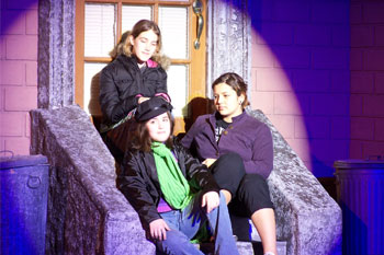 SGM Giotto 400 Spots and SGM Giotto 400 Wash fixtures on an outdoor brick building prop scene with 3 actresses sitting in front of a door on cement stairs with garbage cans on each sides of the stairs  with hues white on performers, purples and reds on the building walls, Goodbye Girl, Osceola Center for the Arts, Kissimmee, Florida, USA